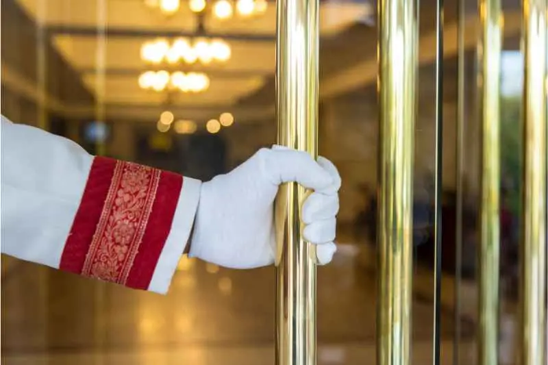 An apartment doorman holding the door open for a resident. 